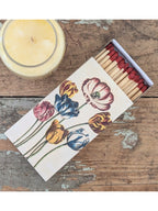 Box of matches with tulips printed on the box on a wooden table next to a candle