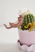 Cactus in a pink pot with a decorative pink ceramic cat on a light gray background