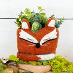 A woolen hand felted pot cover in the form of a sleeping red fox with its tail wrapped around itself.