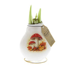 A white waxed amaryllis bulb featuring a printed illustration of red and white mushrooms on autumn leaves. Green amaryllis buds are sprouting, and a brown paper tag is attached to the side.