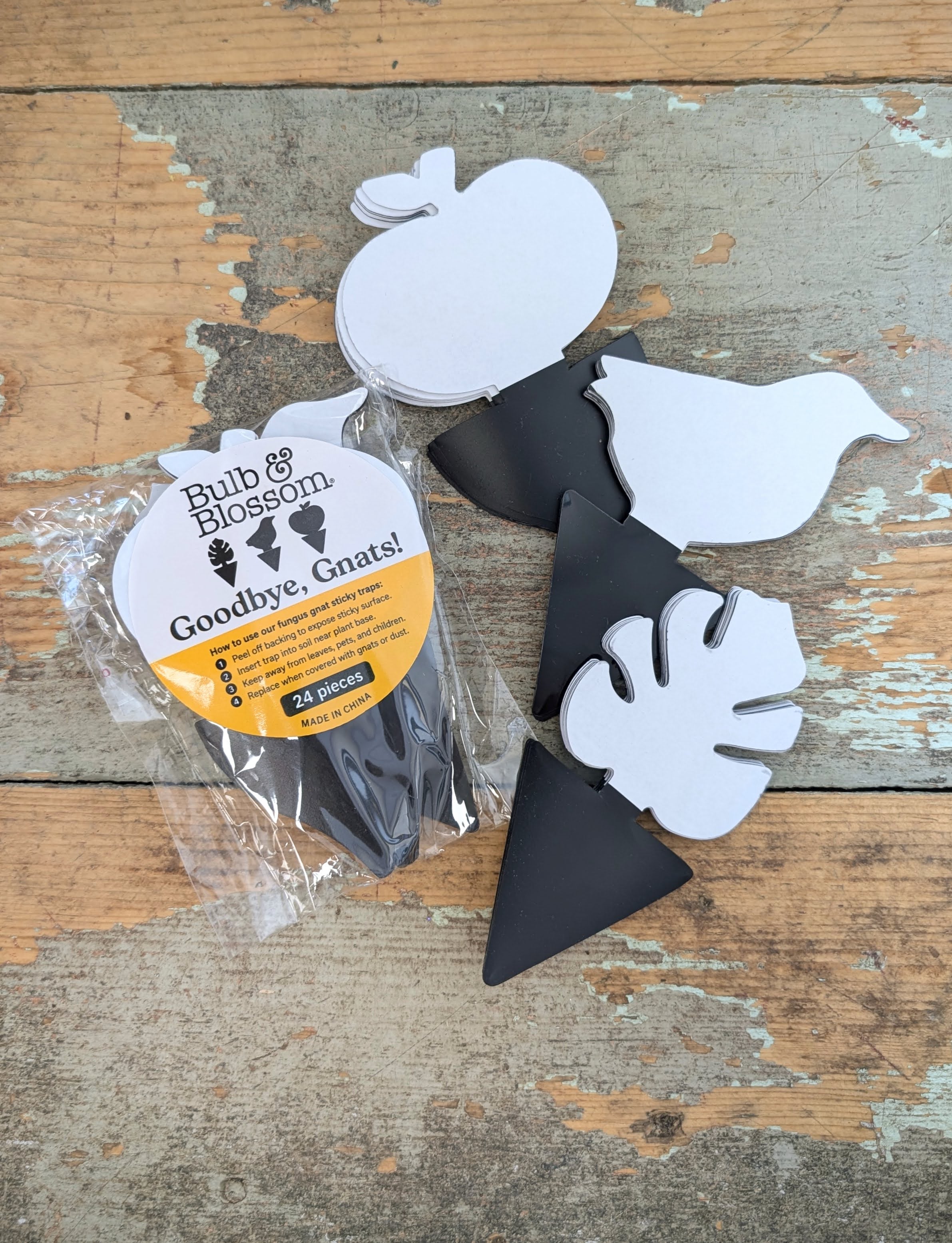 a package of 24 black sticky gnat traps in clear cellophane package labeled "goodbye, gnats!" by Bulb & Blossom. Three shapes of trap are displayed, an apple, a bird, and a monstera leaf.