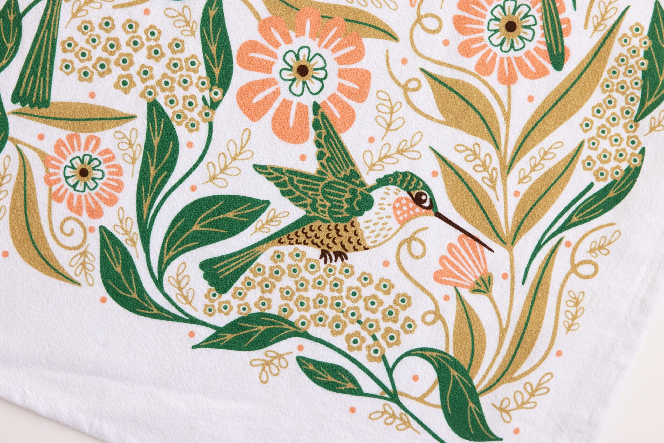 Featuring a green and brown hummingbird with vibrant flowers, leaves, and branches in orange, yellow, and green on white—this Hummingbird Flour Sack Tea Towel adds charm to any kitchen.