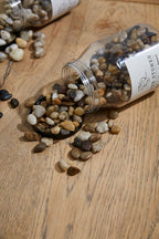 Small bottle of decorative stones spilling onto a wooden surface with a visible brand label.