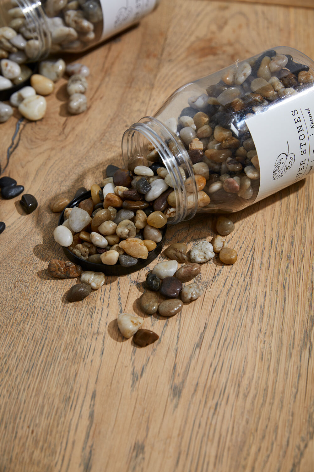 Small bottle of decorative stones spilling onto a wooden surface with a visible brand label.
