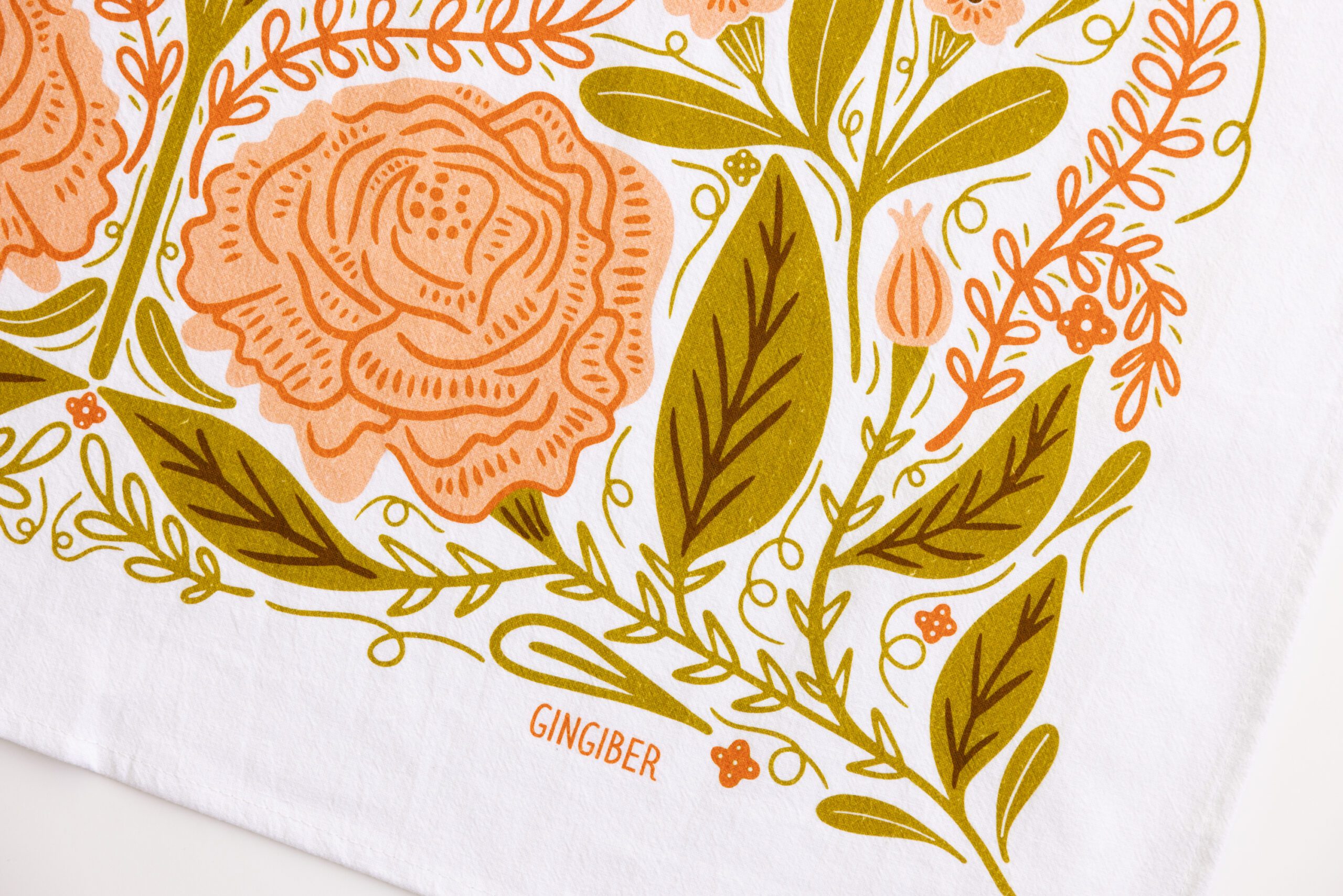 A close-up of the Vintage Butterfly Flour Sack Tea Towel shows an illustrated floral pattern in orange and olive green, with large stylized flowers, leaves, and vines. "GINGIBER" is printed at the bottom center.